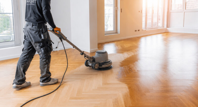 Operario acuchillando suelo de parquet con máquina